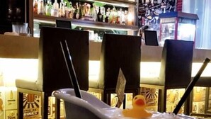 Una bañera con un patito de goma, rodeada de sillas y una zona de bar con botellas.