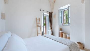 A bedroom with a large bed, a wooden ladder, a window with curtains, and a view of greenery outside.