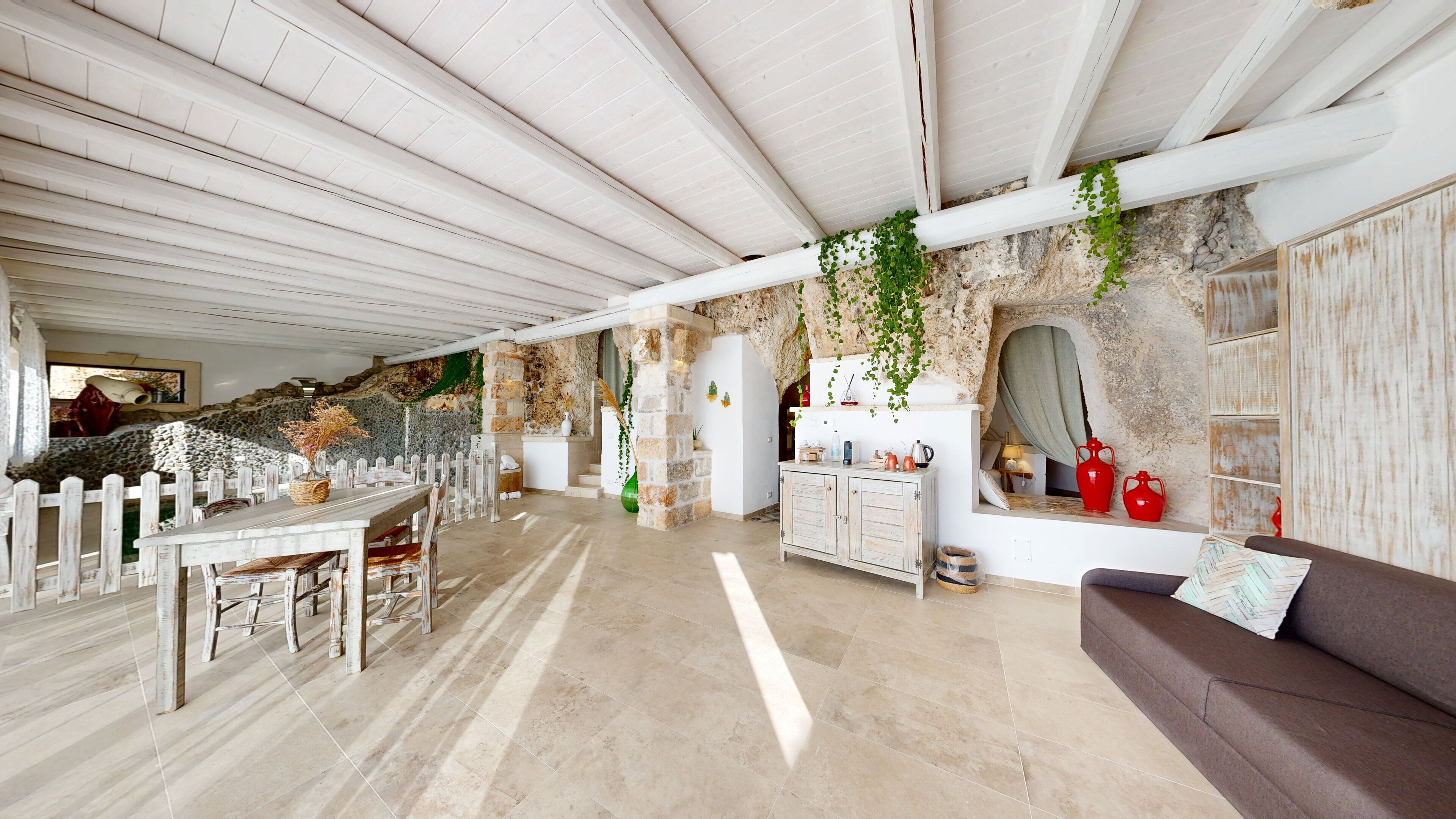 A spacious room with a high ceiling, stone walls, a wooden dining table, and a sofa.