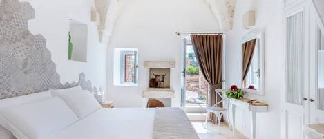 A bedroom with a large bed, a small table with flowers, a view of the outside, and a rustic ceiling.