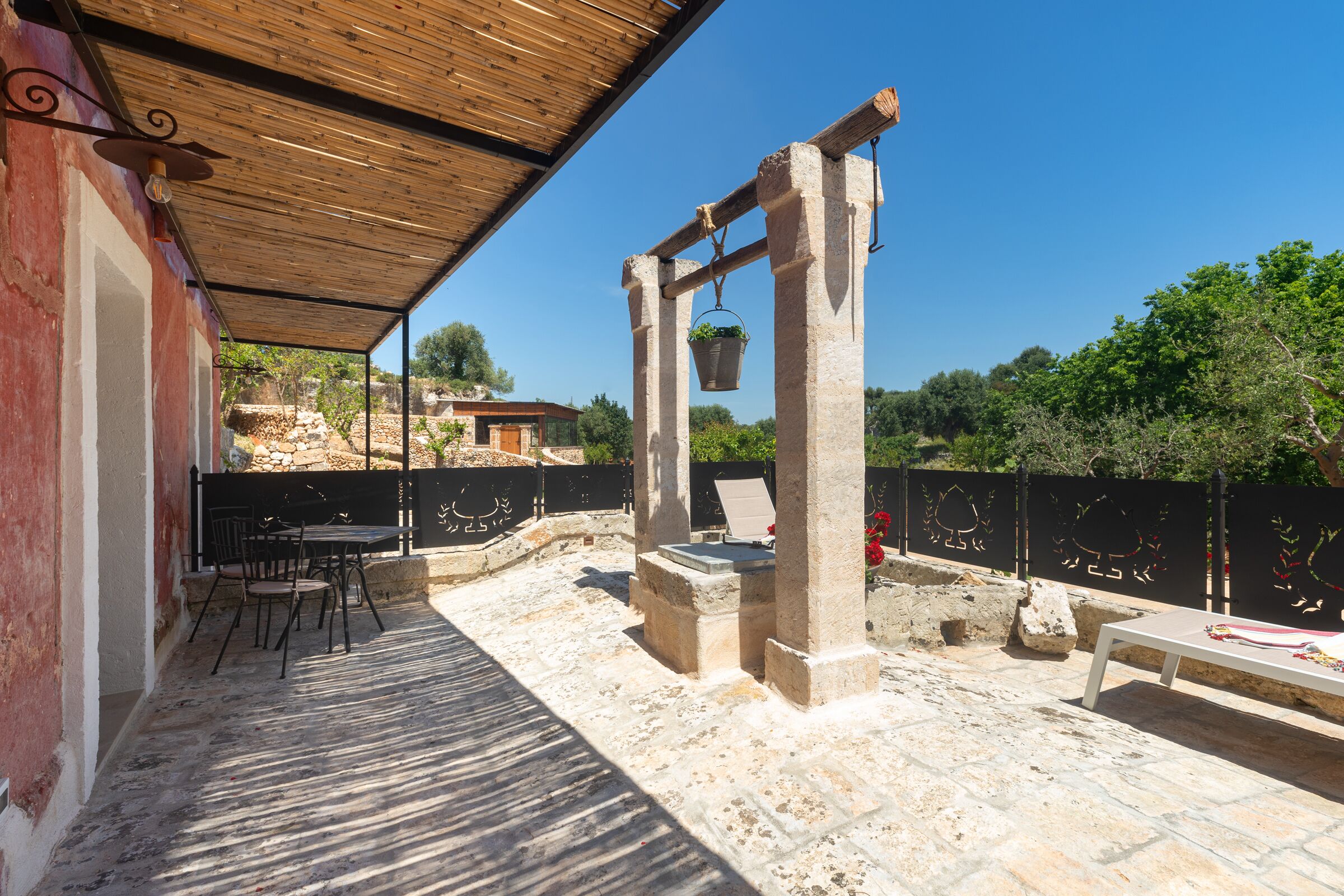 A covered outdoor patio with stone flooring, a table and chairs, and a hanging planter.