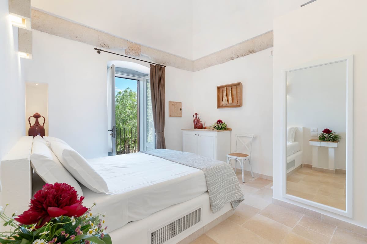 A bedroom with a bed, a desk, a chair, and a large mirror.