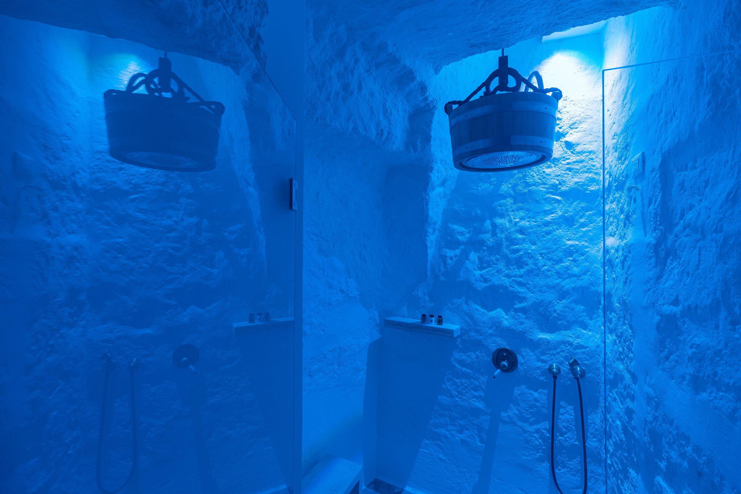 Ein Zimmer mit Steinwand, einem von der Decke hängenden Eimer und einem Duschbereich mit Schlauch.