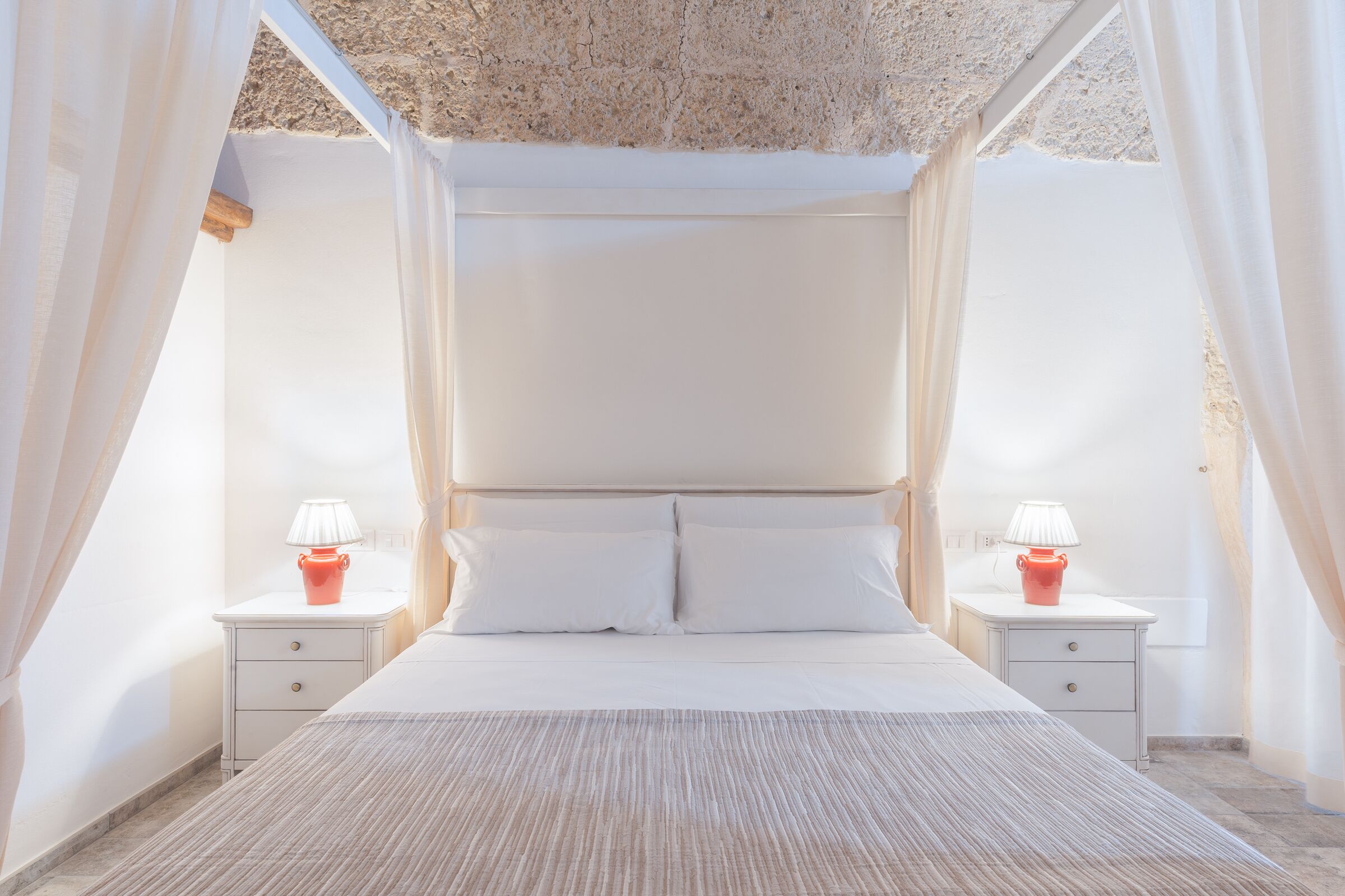 A bedroom with a canopy bed, two bedside tables with lamps, and a textured ceiling.