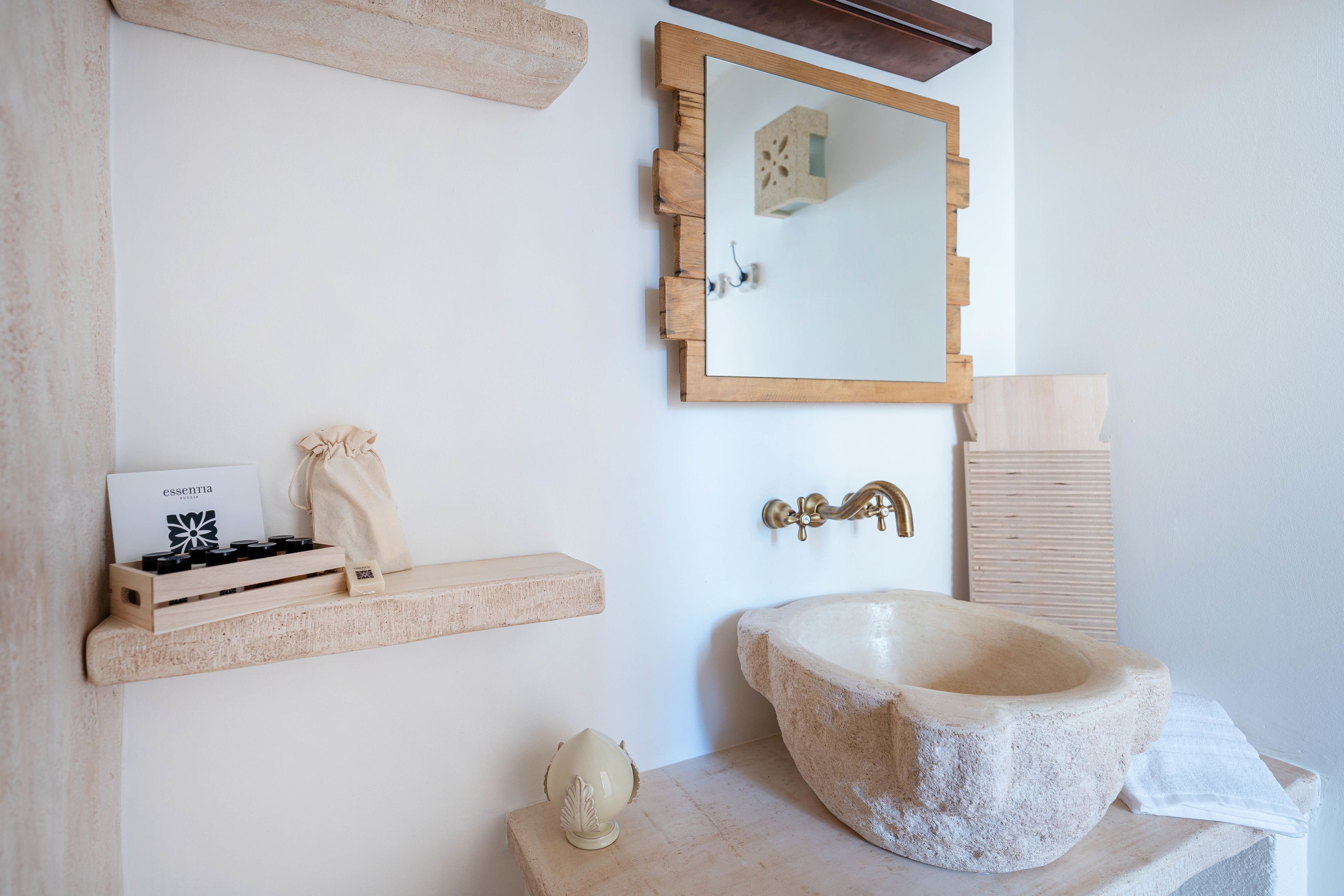 Ein Badezimmer mit einem Steintonne, einem Holzregal mit Toilettenartikeln und einem Spiegel mit Holzrahmen.
