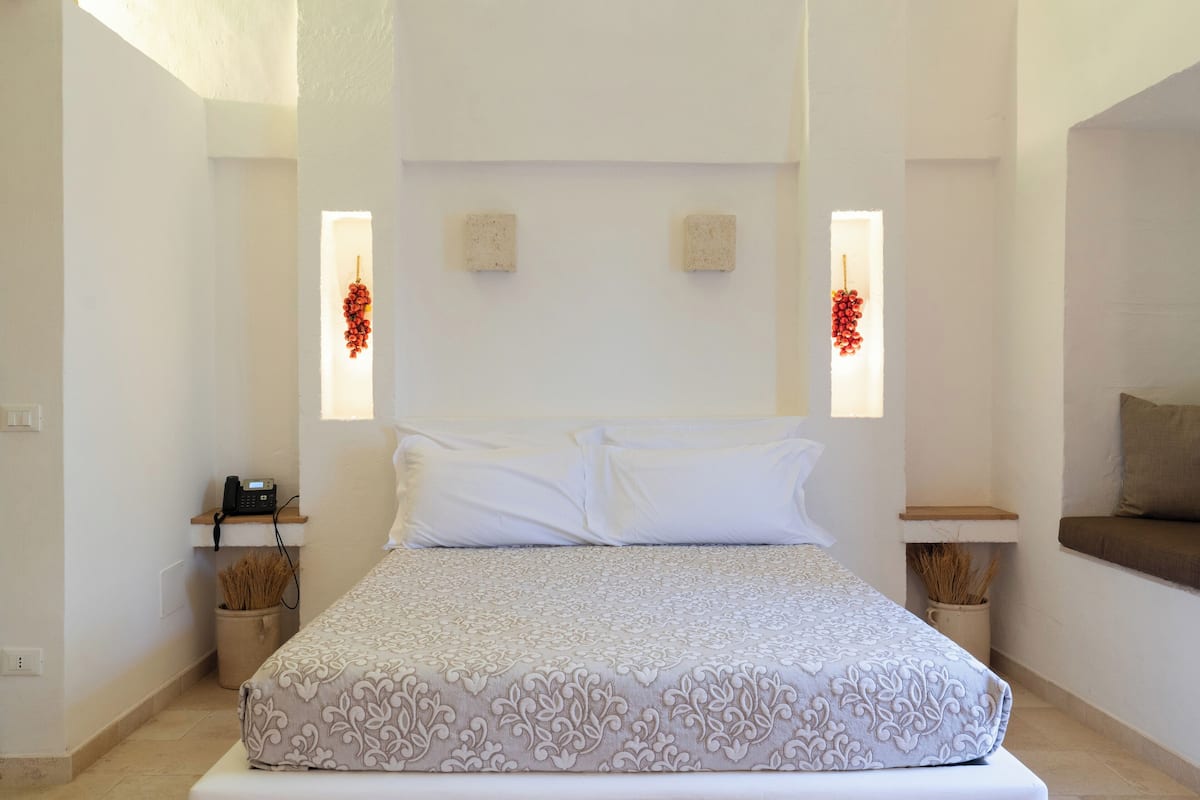 A bedroom with a large bed, two bedside tables, a telephone, and a window with red decorations.