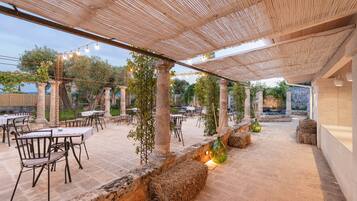 Un patio al aire libre con mesas y sillas, una pérgola con luces colgantes y un camino de piedra.