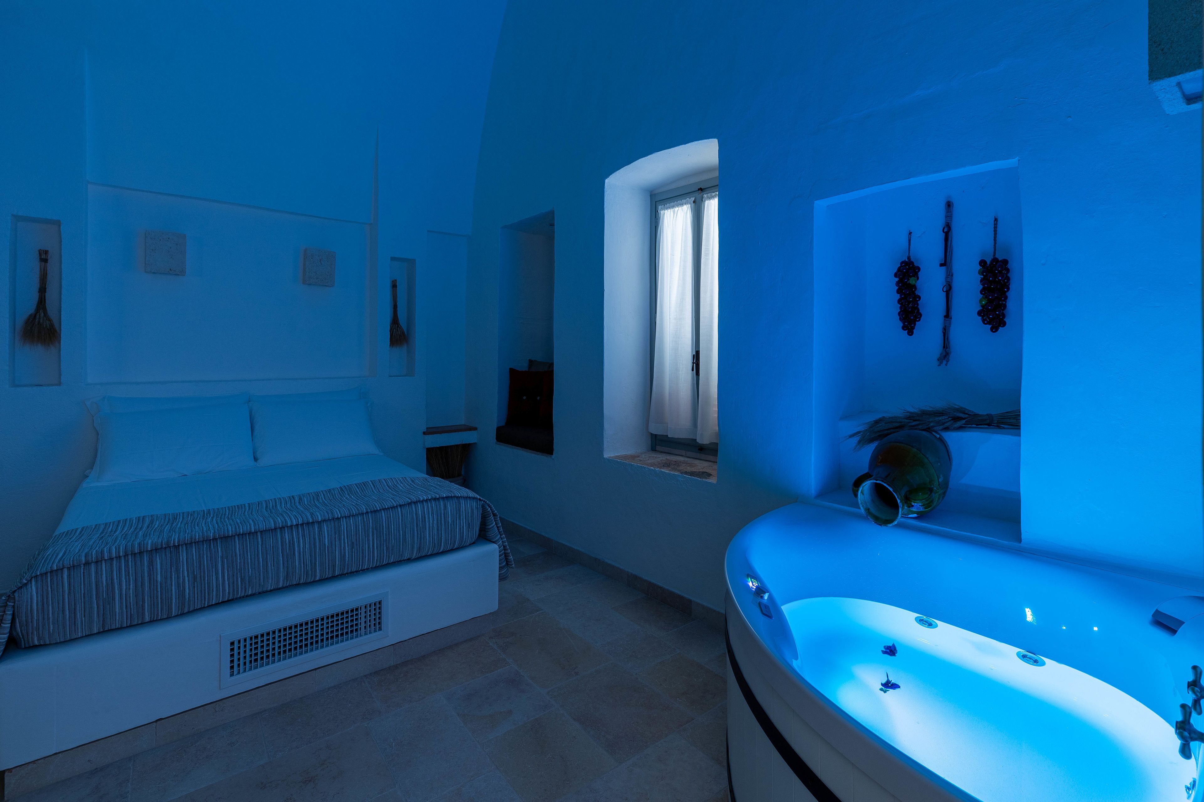 A modern bedroom with a large bed, a window with curtains, a built-in bathtub, and wall-mounted artwork.