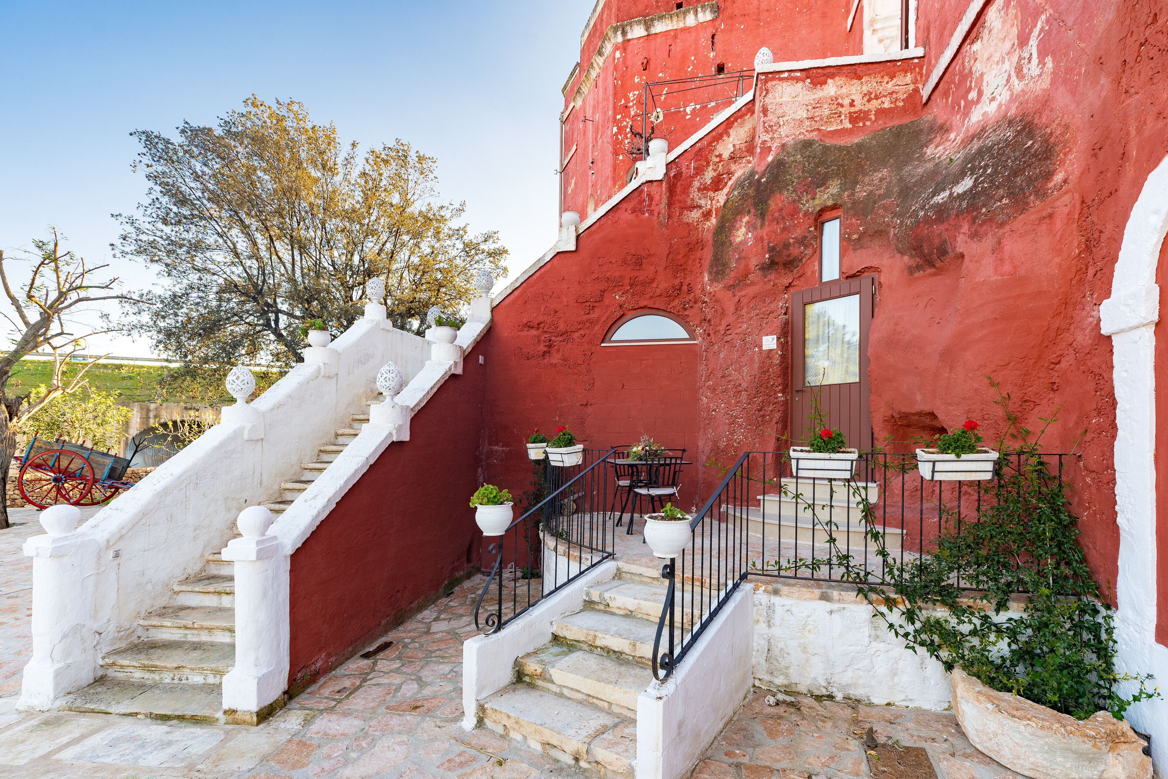 A red building with white steps and railings, outdoor seating, and potted plants.