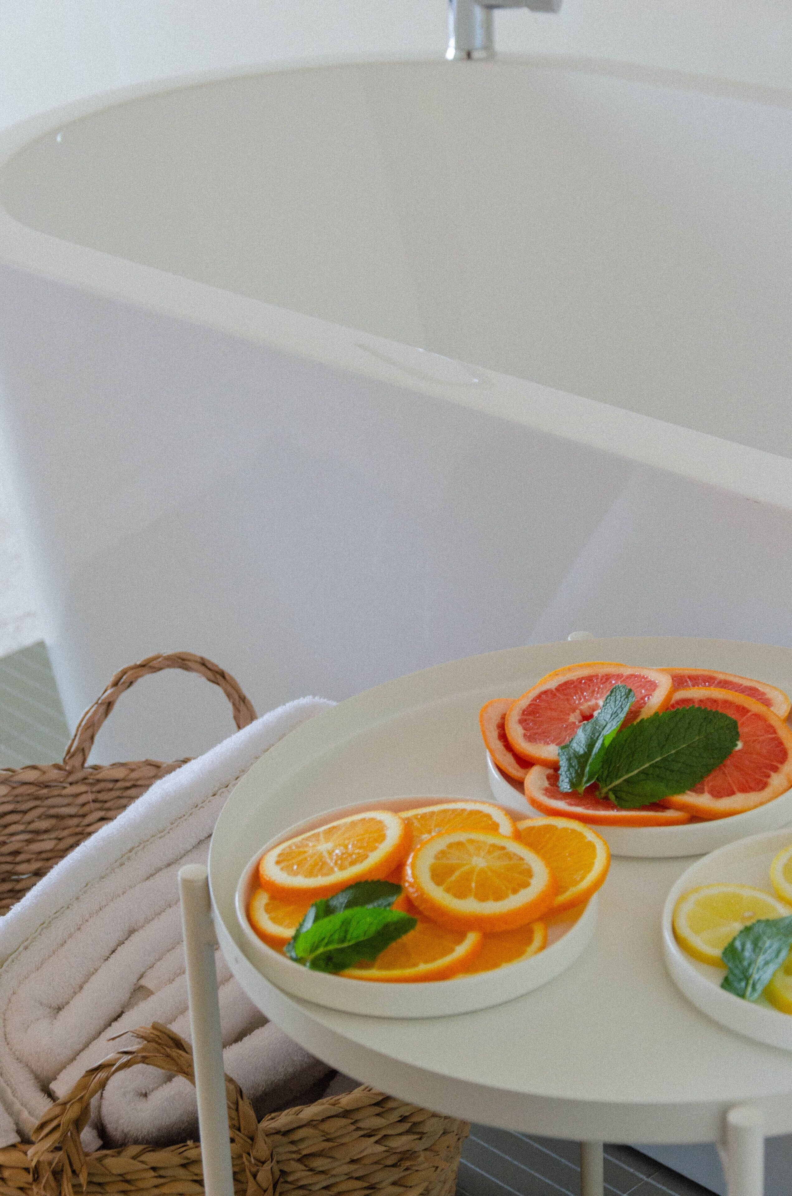 Um banheiro com banheira, uma mesa branca com fatias de fruta e uma cesta de palha com uma toalha.
