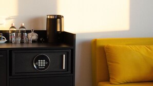 En sort minibarskab med kaffemaskine, glas og flasker, en gul sofa og et tæppe på gulvet.