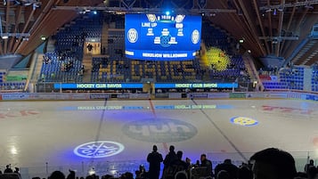 An indoor ice hockey arena with a scoreboard, empty spectator seats, and a hockey rink.
