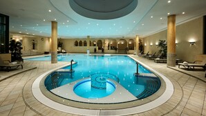 Ein Innenpool mit einem zentralen Whirlpool, umgeben von Liegestühlen und einer Decke mit Oberlicht.