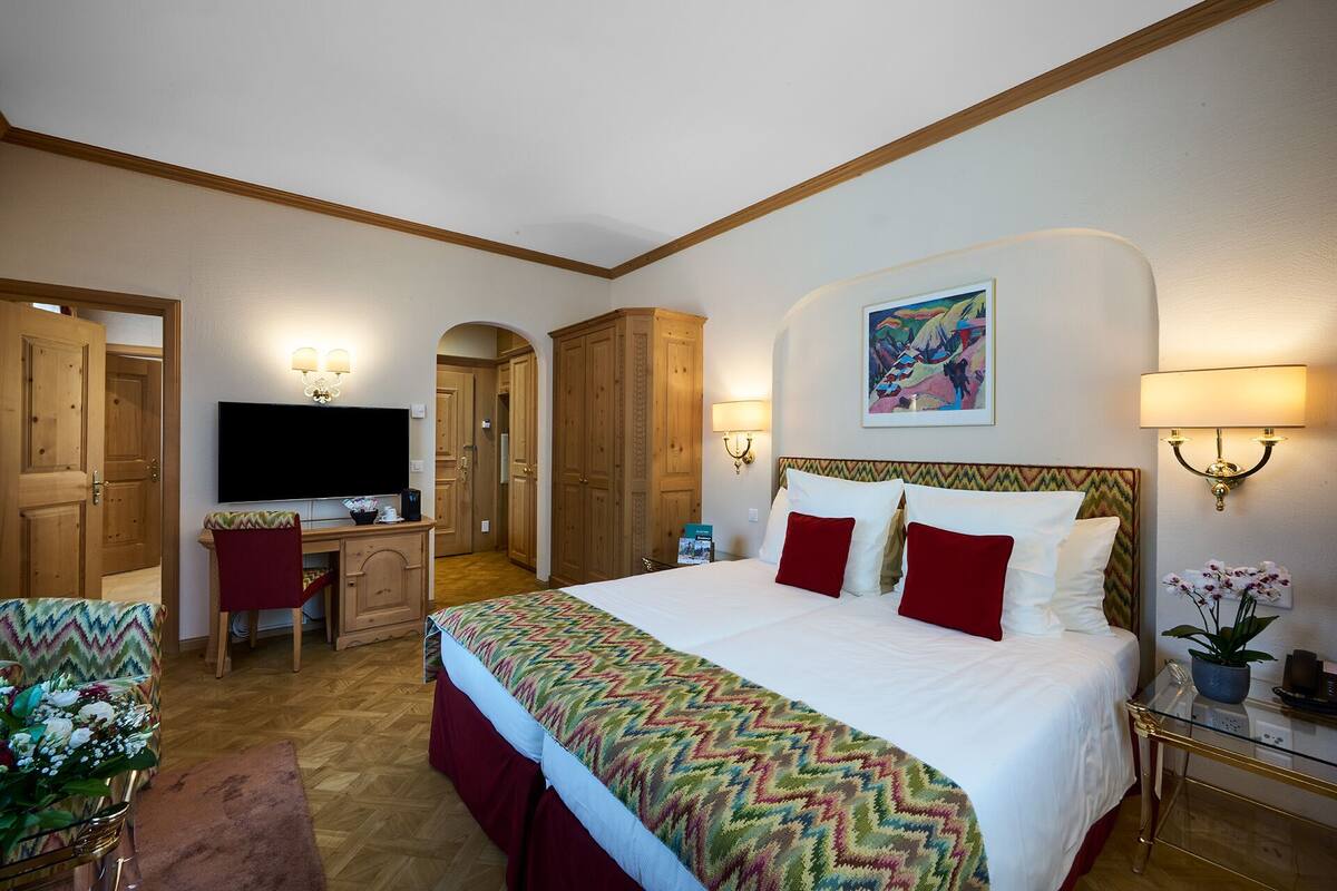 Une chambre d’hôtel avec un grand lit, un bureau avec une télévision, une chaise et une petite table avec une plante.