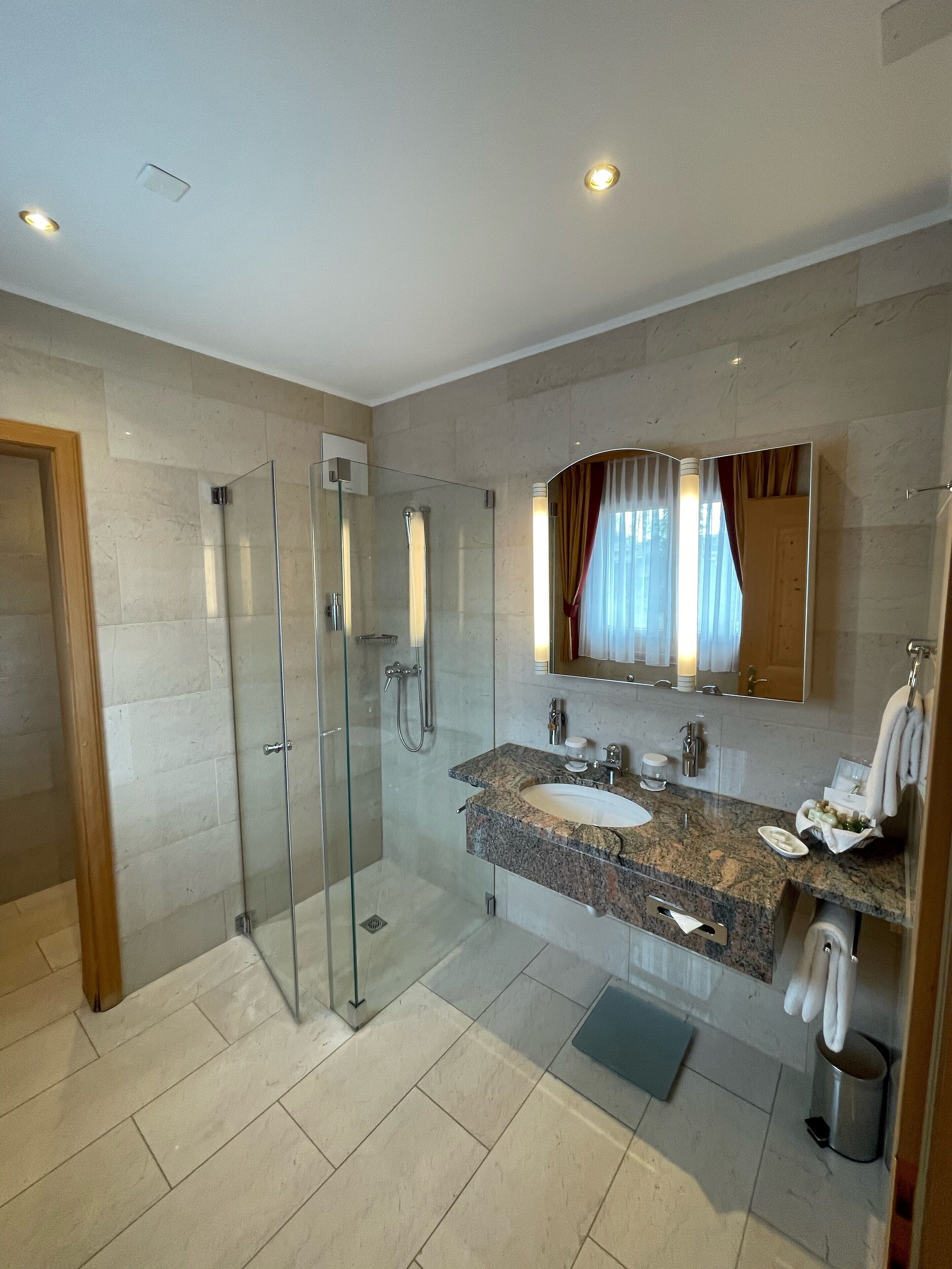 A modern bathroom with a glass-enclosed shower, a granite sink, and a large mirror.