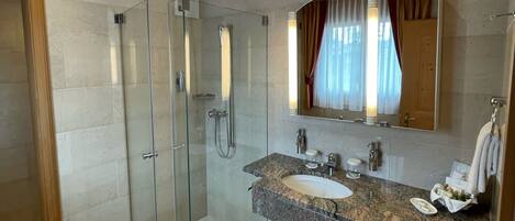 A modern bathroom with a glass-enclosed shower, a granite sink, and a large mirror.