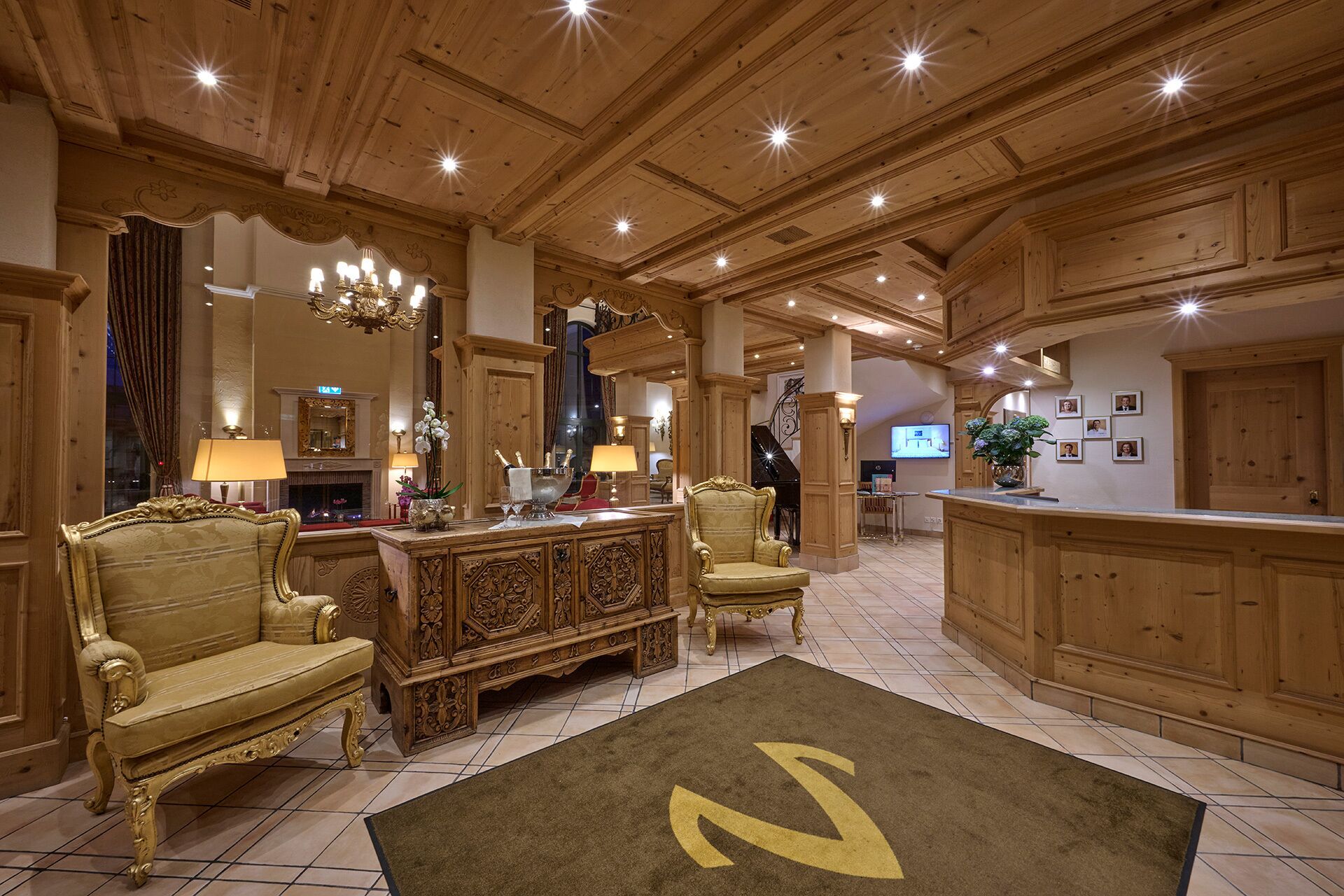 A lobby with a grand chandelier, ornate wooden furniture, a piano, and a reception desk.