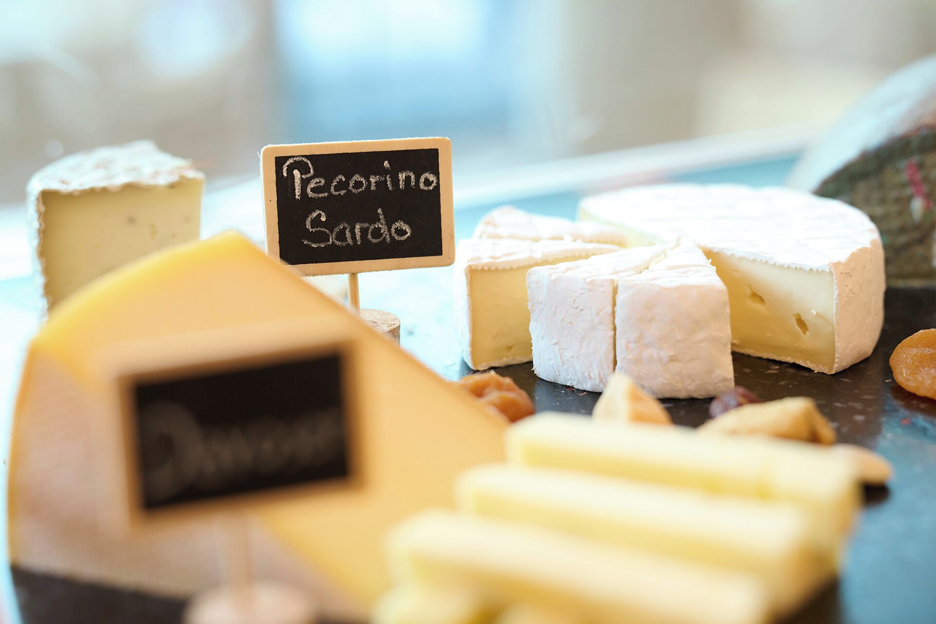 Variedad de quesos, incluyendo Pecorino Sardo, con un cartel de pizarra que indica el tipo.