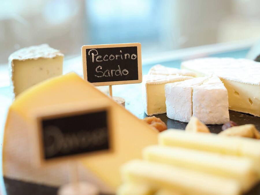 Variedad de quesos, incluyendo Pecorino Sardo, con un cartel de pizarra que indica el tipo.
