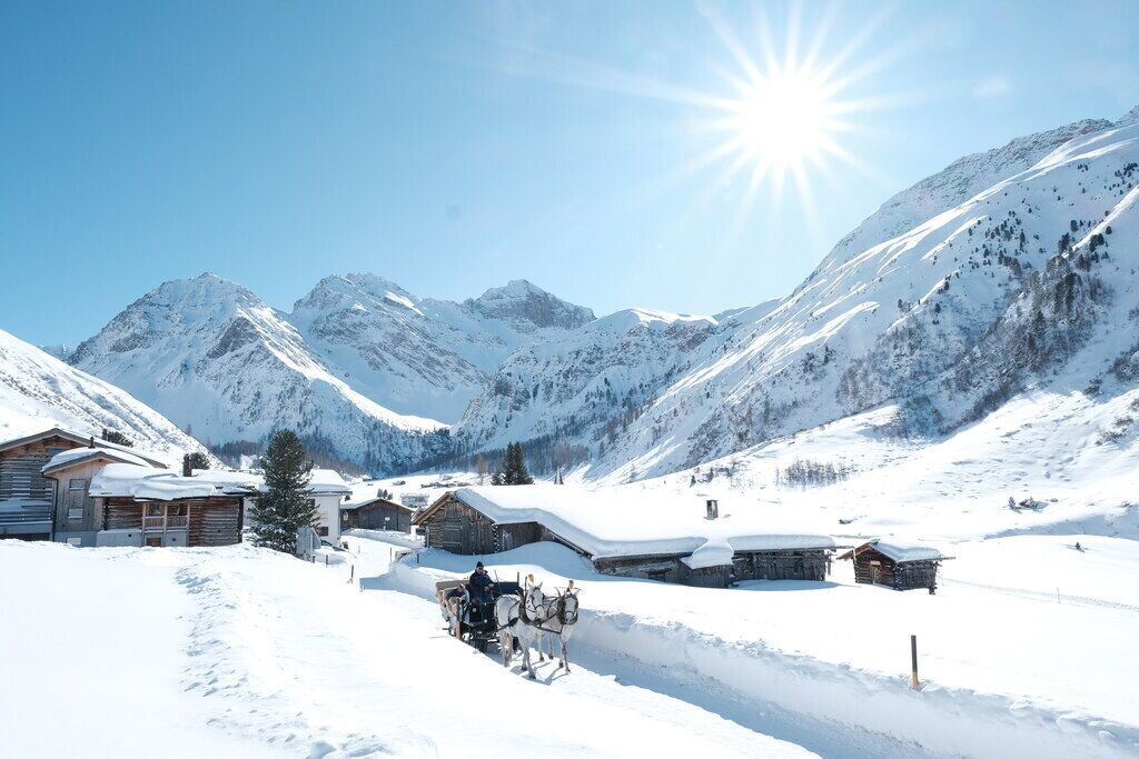 Un village de montagne enneigé, avec des chalets en bois et un traîneau tiré par des chevaux.
