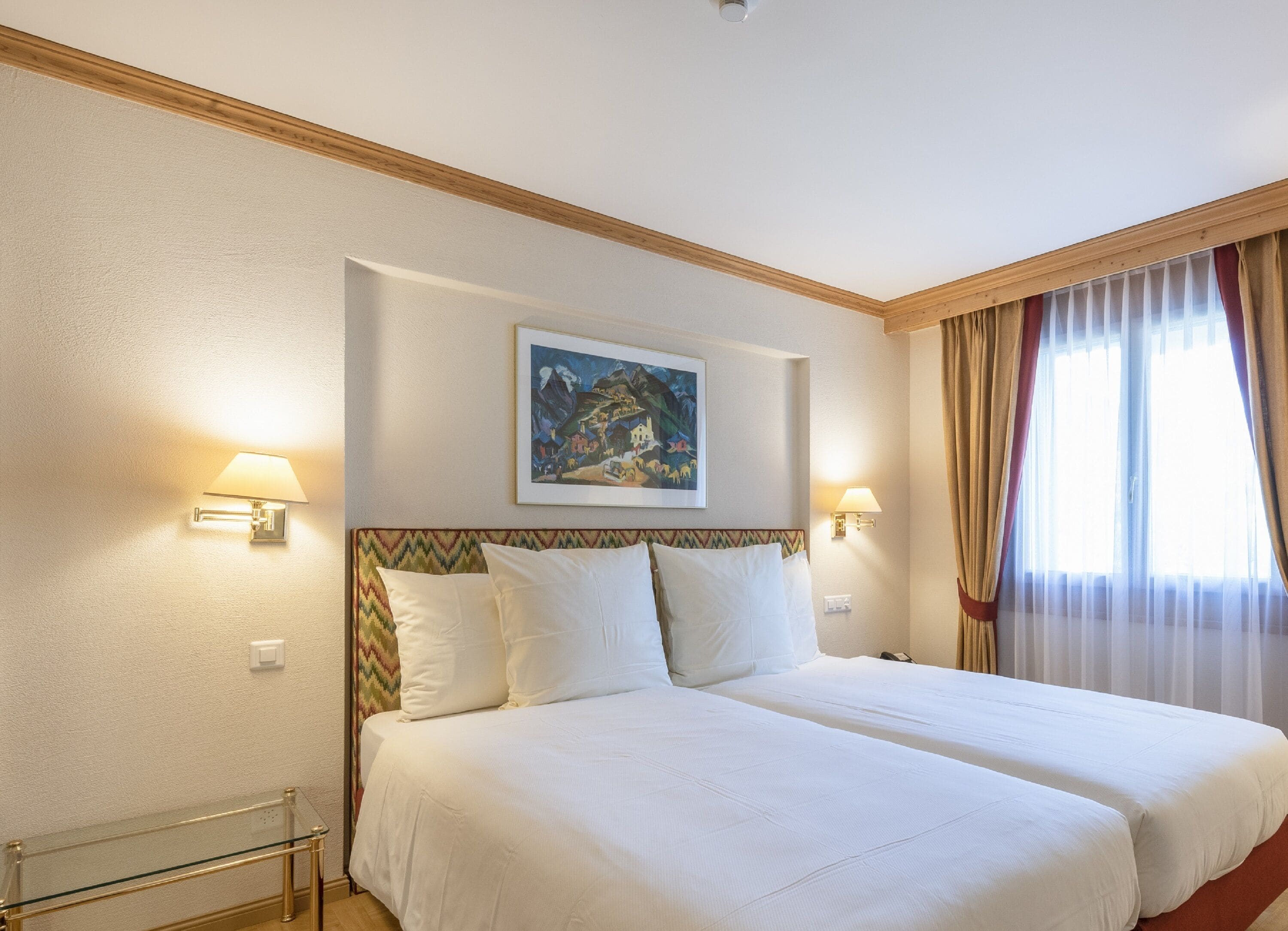 A hotel room with a large bed, two bedside lamps, a painting on the wall, and a window with curtains.