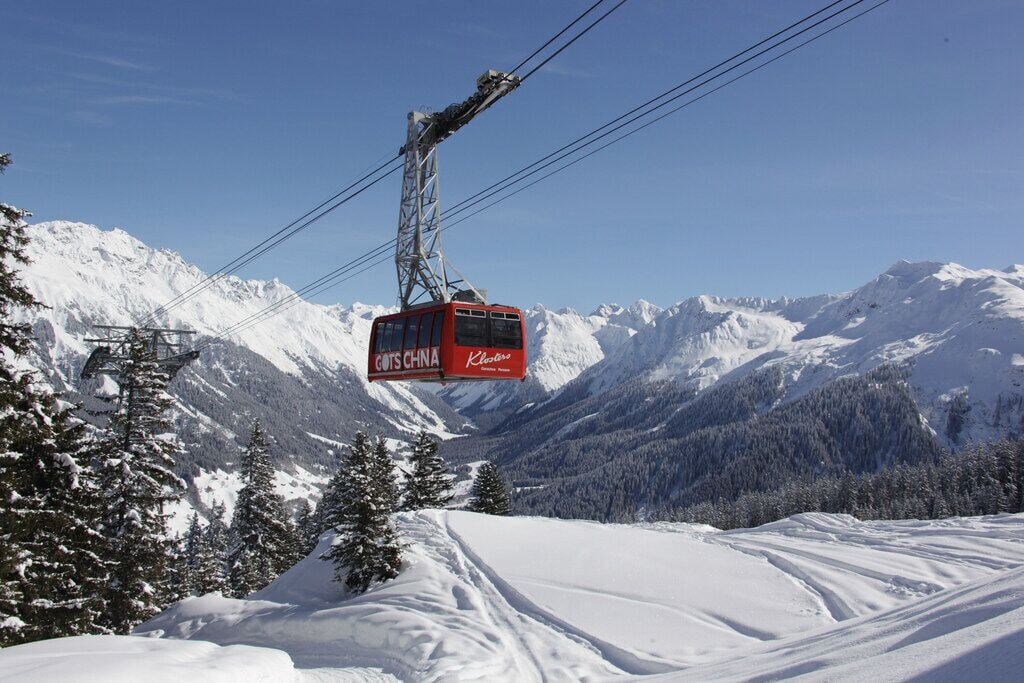 Un teleférico con la etiqueta "GOTS CHINA" suspendido sobre un paisaje montañoso nevado.
