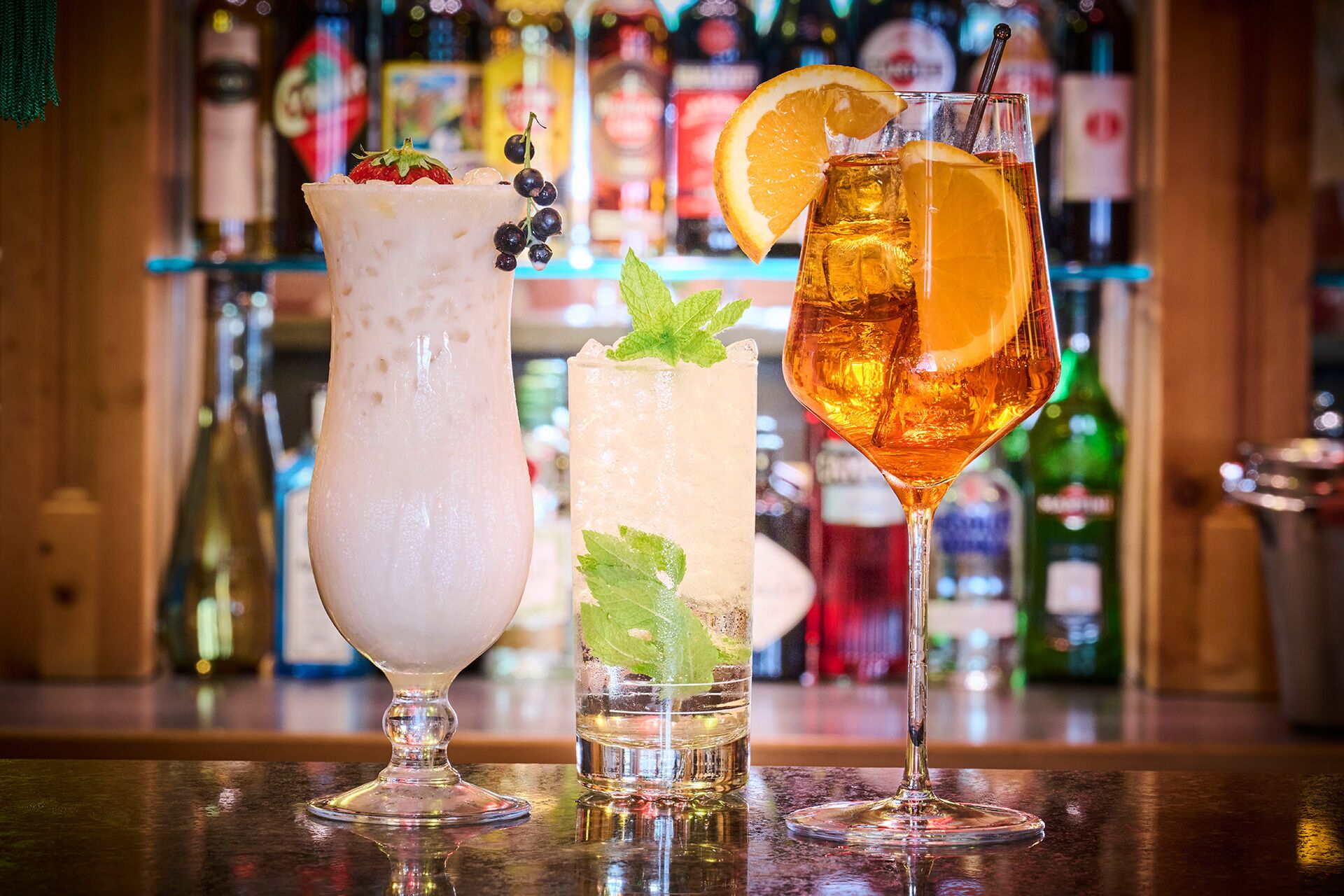 Three drinks on a bar counter with a blurred background of bottles.