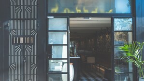 Entrada de un hotel con suelo a cuadros, puerta metálica decorativa y un interior visible con mostrador y sillas.