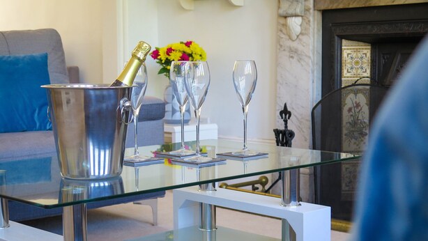 Ein modernes Wohnzimmer mit einem Glastisch, einem Champagnerkübel aus Metall und drei Weingläsern.