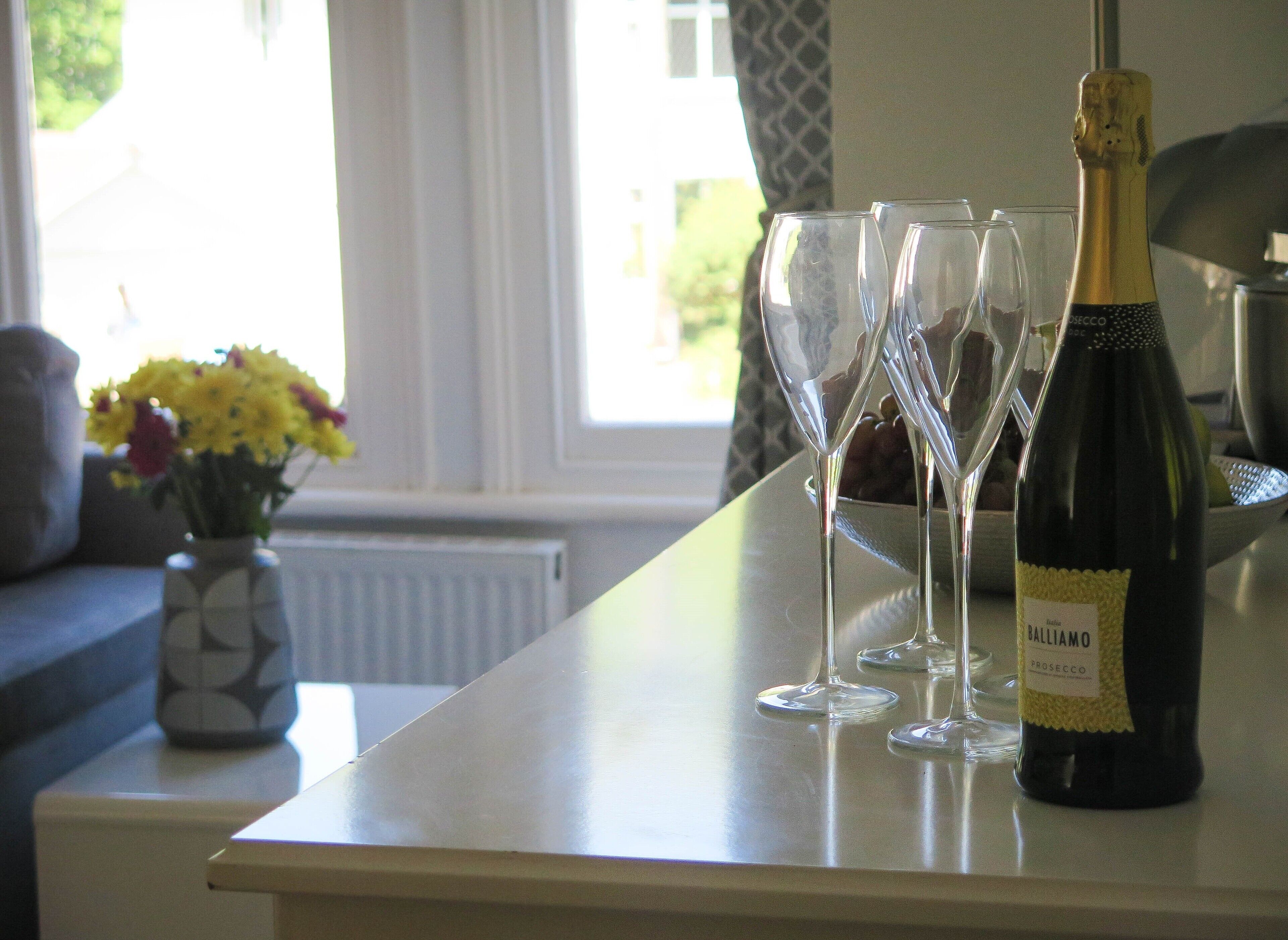 A bottle of Balliamo Prosecco on a table with three empty wine glasses.