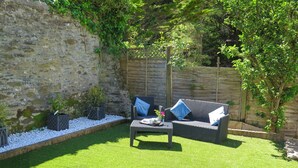 Ein Patio mit Korbsessel-Sofa, einem kleinen Tisch und Kübelpflanzen.
