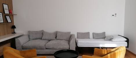A modern living room with a grey sofa, two yellow armchairs, a black coffee table, and a white bed.