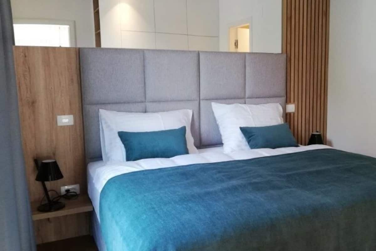 Una habitación de hotel moderna con una cama grande, una mesita de noche de madera y una lámpara.