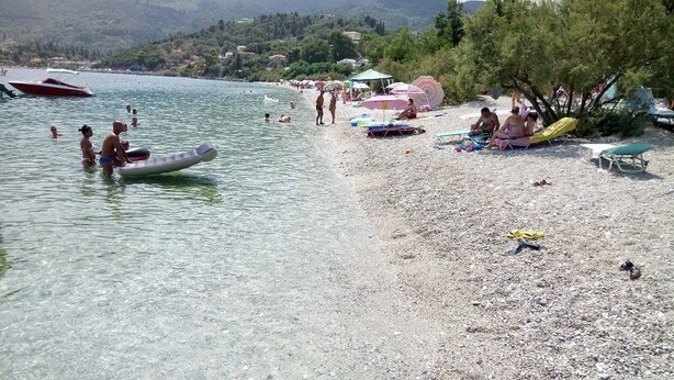 Una playa con gente nadando y tomando el sol, barcos en el agua y sombrillas en la arena.