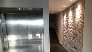 A hallway with a metallic elevator and a stone wall with recessed lighting. - Montreux Grand Rue Apartments (Montreux)