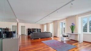 A spacious living area with a wooden floor, a gray sofa, a white desk, and a large window providing natural light. - Montreux Grand Rue Apartments (Montreux)