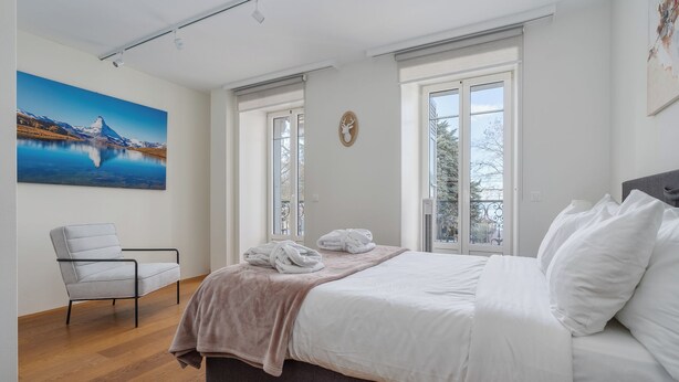 A bedroom with a bed, a chair, and a painting of a mountain landscape. - Montreux Grand Rue Apartments (Montreux)