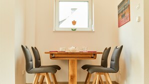 Een eettafel met twee stoelen, een raam met uitzicht op een bloem en een schilderij aan de muur.