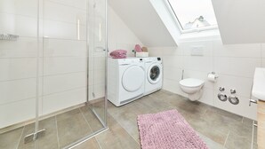 Een moderne badkamer met een douchecabine van glas, een wasmachine, een toilet en een dakraam.