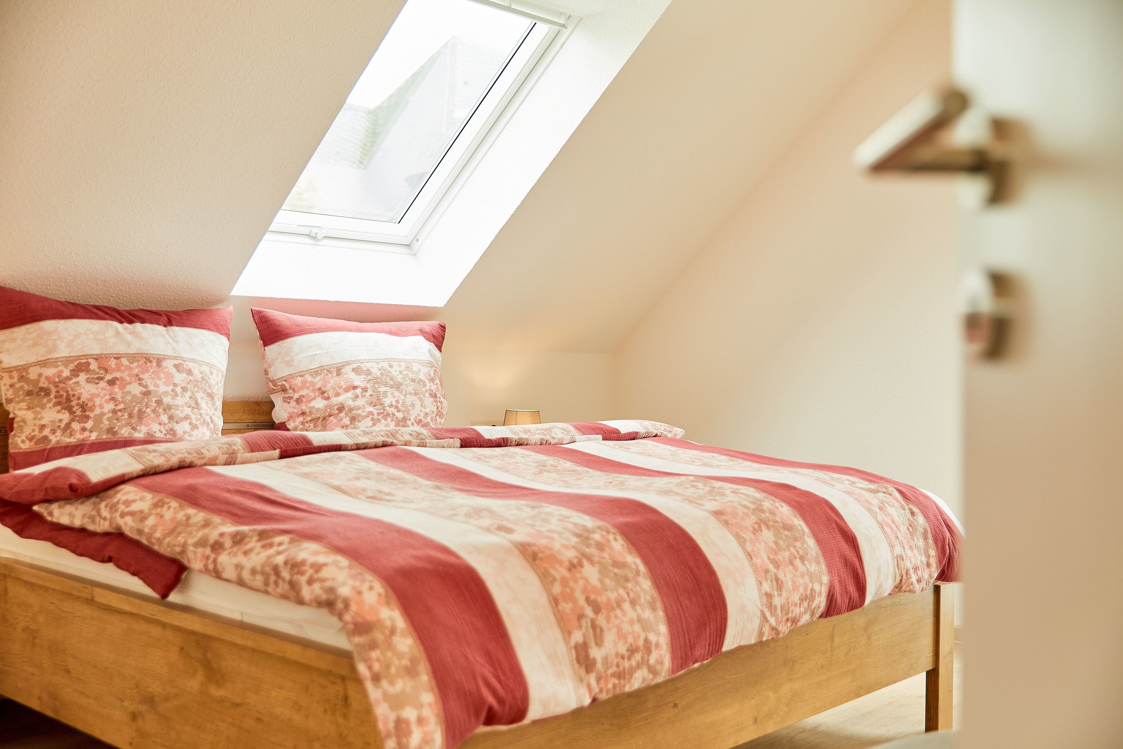 A bedroom with a sloped ceiling, a wooden bed frame, and a patterned bedspread.