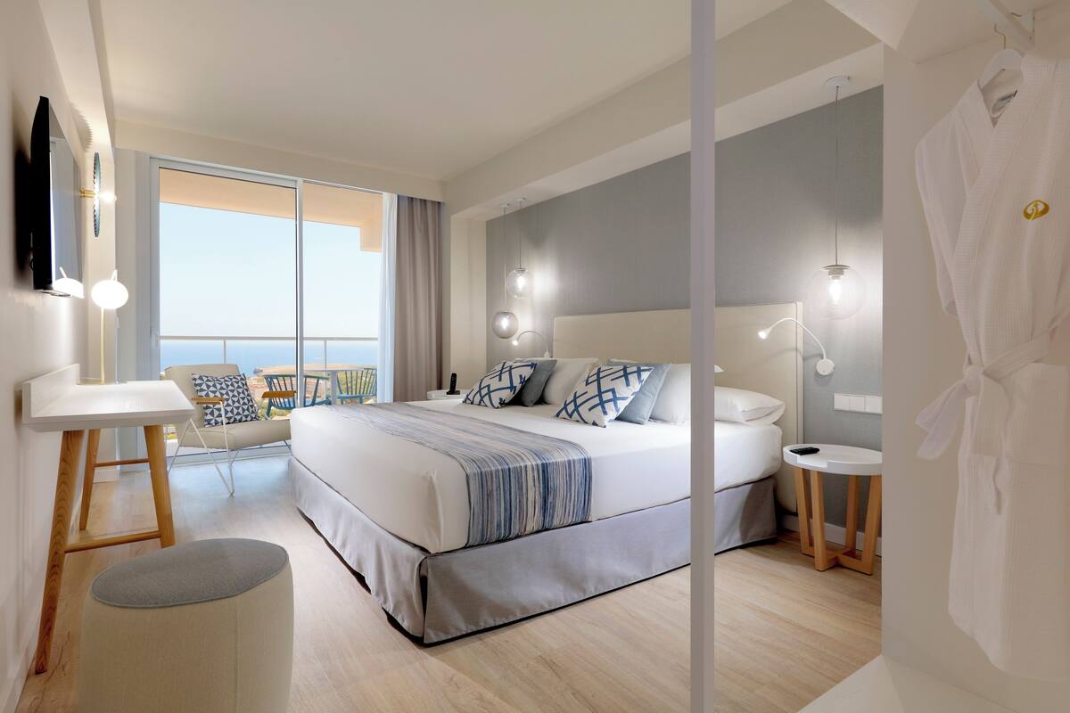 A modern hotel room with a large bed, bedside tables, a desk, and a view of the outdoors.