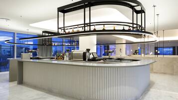 A modern bar area with a curved counter, a glass shelf with bottles, and a seating area with a view of the city.