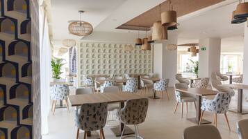 A modern dining area with multiple tables and chairs, a patterned wall, and hanging wicker lamps.