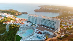 An aerial view of a hotel with a pool, multiple buildings, and a coastal backdrop. - Palladium Hotel Menorca (Mercadal)