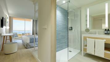 A modern hotel room with a glass-enclosed shower, a large mirror, a wooden vanity, and a balcony with a view.