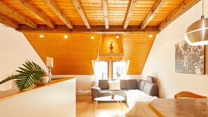 A cozy loft-style living space with a sloped ceiling, wooden beams, a gray sofa, a white coffee table, and a dining area. - Altes Eichamt (Bernkastel-Kues)