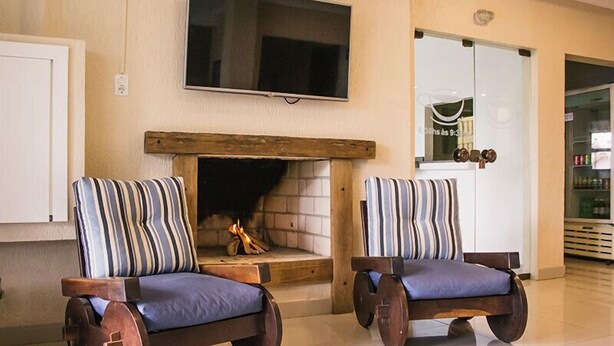 Two rocking chairs with striped cushions in front of a fireplace with a TV above it. - Hotel Guaíba (Guaiba)