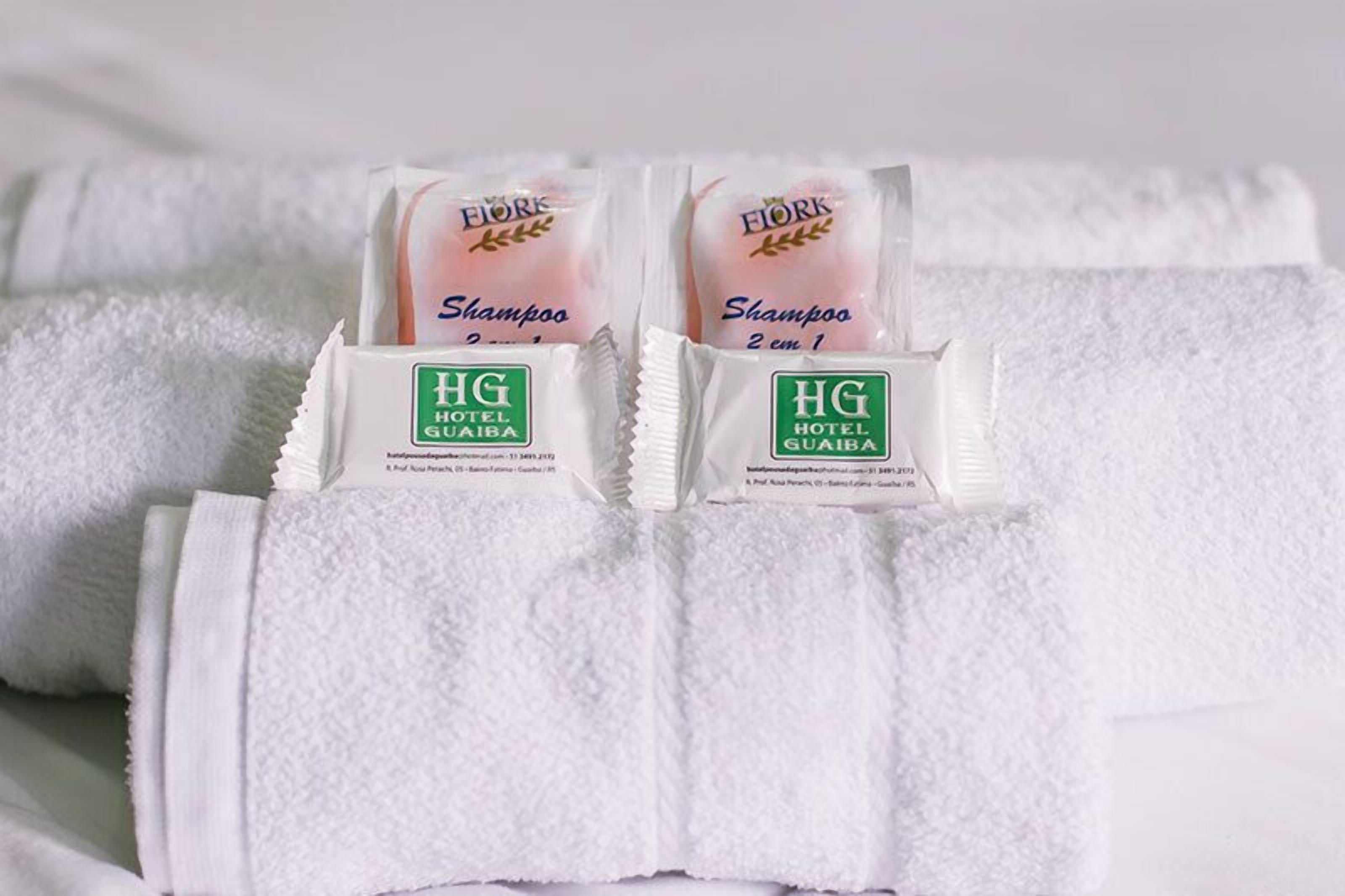 Dos botellas de champú HG Hotel Guaiaba sobre una toalla blanca.