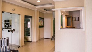 A hotel lobby with a reception desk, a refrigerator, and a door leading to a hallway. - Hotel Guaíba (Guaiba)