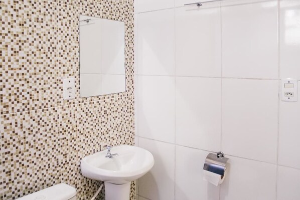 A bathroom with a mosaic tile wall, a white sink, a mirror, and a toilet paper holder.